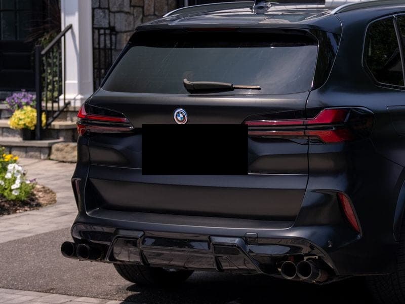Same matte-black BMW X5 parked clean in the same driveway, deep gloss across the rear tailgate and diffuser, license plate obscured.