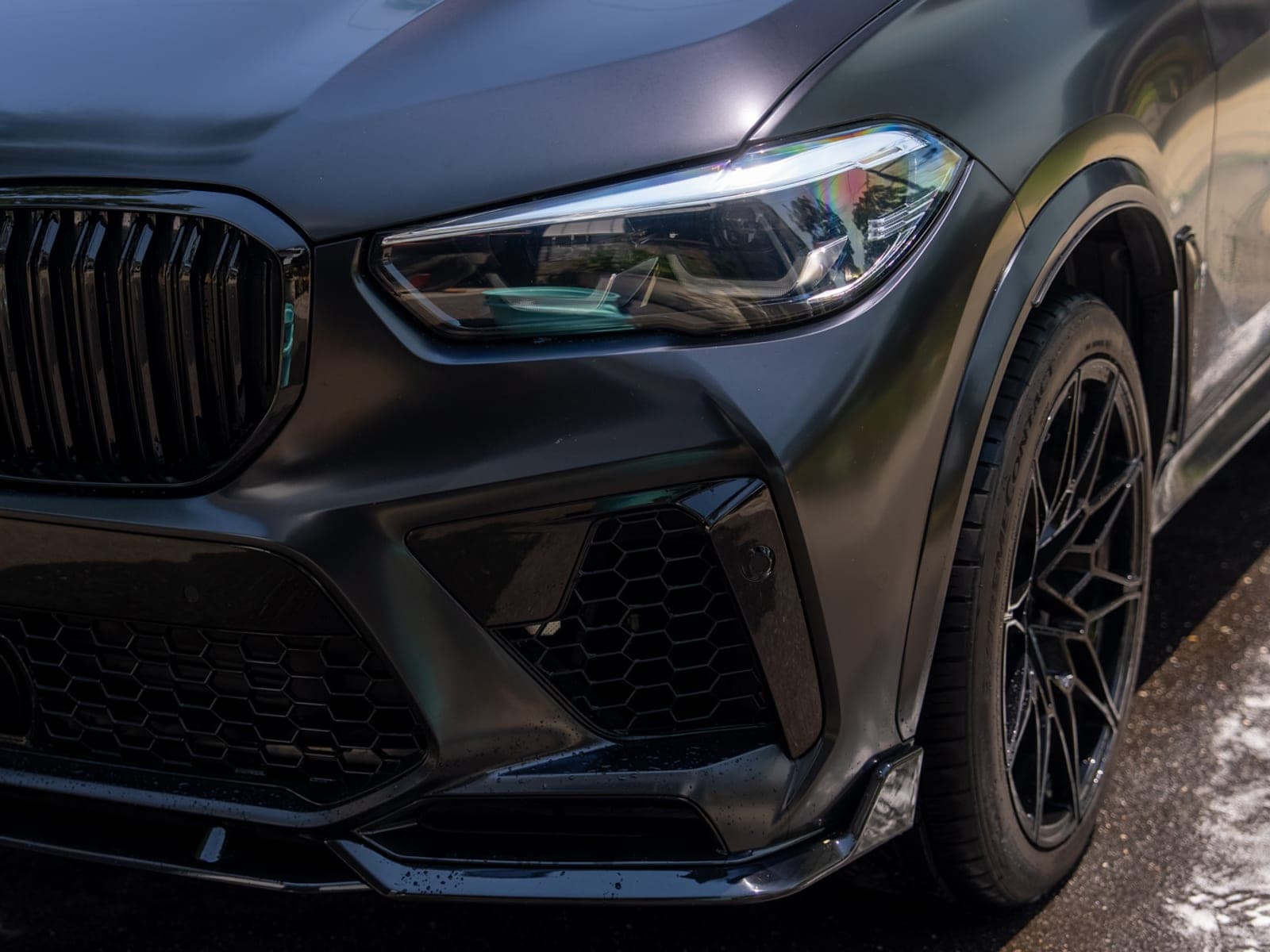 Front quarter panel of a matte-black BMW X5M after ceramic protection, showing gloss depth across the hood and headlight.
